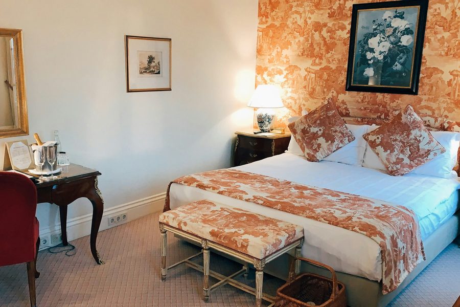 Classic bedroom with a coral toile feature wall behind the bed, matching toile bedding and a red velvet chair