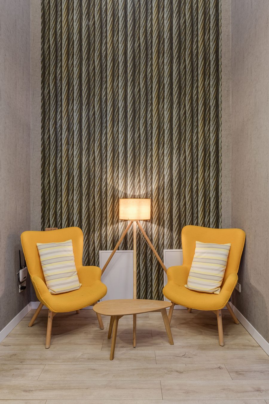 Seating nook with two mustard armchairs and a tripod lamp in front of a vertical textured-stripe accent wall