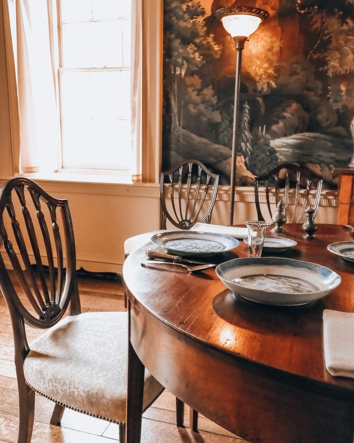 Classic dining room with a hand-painted scenic landscape wallcovering, shield-back chairs and a polished wood table set with blue and white plates